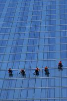 Vijf hardwerkende glazenwassers aan het werk op een blauw modern hoog gebouw
