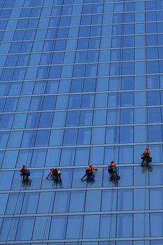 Cinq laveurs de vitres au travail sur un grand immeuble moderne bleu.