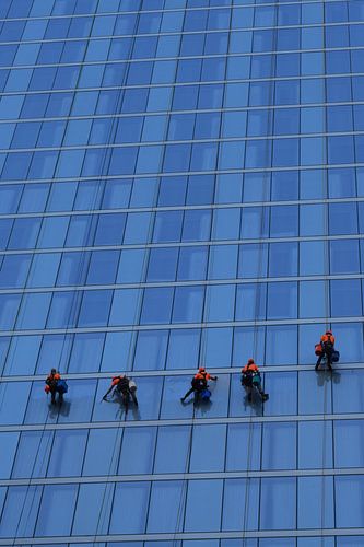 Fünf fleißige Fensterputzer bei der Arbeit an einem blauen modernen Hochhaus