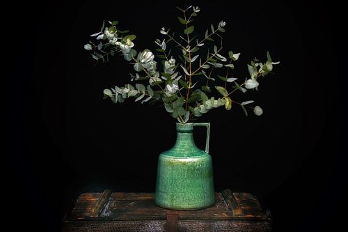 Groene kan met eucalyptus op een oude kist