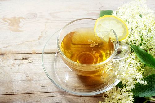 Elderflower tea with lemon and some blossoms on a rustic wooden table, natural home remedy for blood