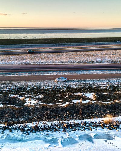 Auto op Afsluitdijk tussen ijs en Waddenzee
