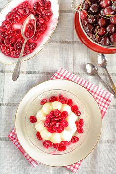 A pudding with freshly cooked cherry compote stands on a plate by Edith Albuschat