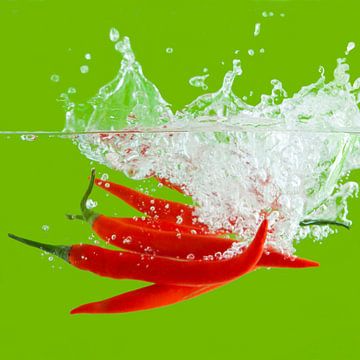 Contrastrijke foto van rode pepers vallend in het water van Henny Brouwers