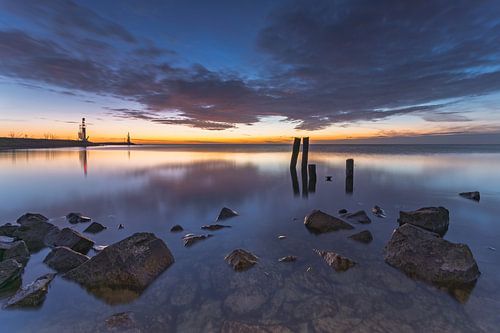 Rustige zonsopkomst bij Den Oever aan het IJsselmeer met stenen, houten palen en vuurtoren in de verte