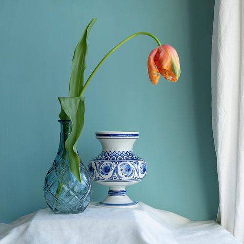 Stilleven met oranje tulp in blauwe vaas en lege delfts blauwe vaas blauwe achtergrond