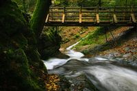 Snelstromende rivier onder een houten brug.