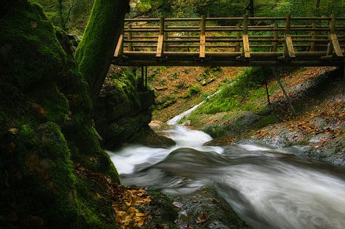 Snelstromende rivier onder een houten brug.
