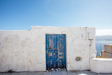 Wit huisje met blauwe deur tegen een blauwe lucht in Santorini, Griekenland van WorldWidePhotoWeb