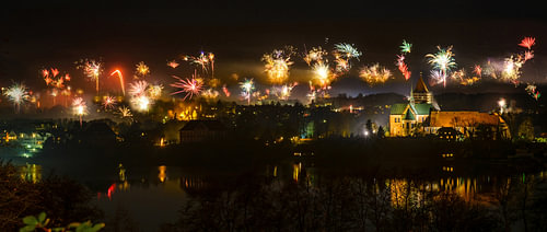Neujahrsfeuerwerk über der Altstadt von Ratzeburg bei Nacht mit beleuchtetem Dom und Spiegelungen im