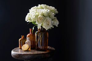 Stilleben mit weißen Rosen in braunen Flaschen und Zitrone