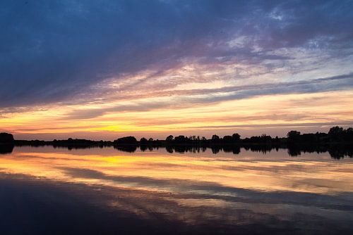 Weerspiegeling van de lucht in het water. Gouden, gele en roze tinten van de lucht worden weerspiegeld in het meer.