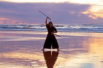 Jonge samurai vrouw met japans zwaard (katana) op het strand bij zonsondergang van Eye on You