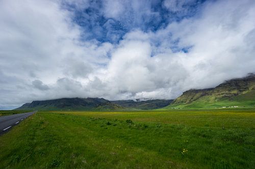 IJsland - Met wolken bedekte groene vulkanische bergen achter weiland