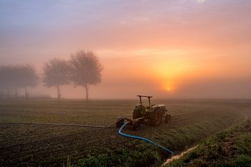 Un tracteur pompe l'eau d'un fossé pendant un lever de soleil brumeux sur Moetwil en van Dijk - Fotografie