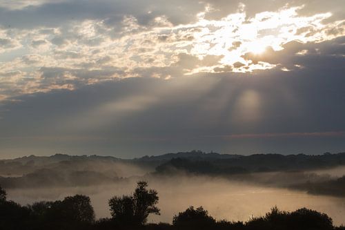Zon door wolken boven mist duinlandschap