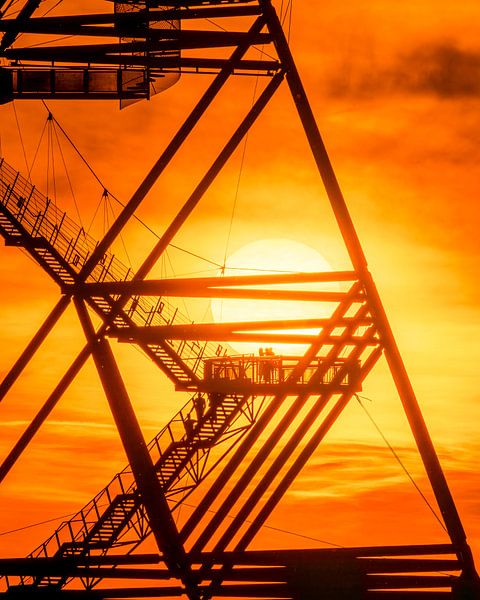 Die grafische Klarheit des Tetraeders im Kontrast zu den warmen Farben des Sonnenuntergangs erzeugt ein faszinierendes Zusammenspiel von Form, Licht und Silhouetten. Es ist ein Bild, das die Schönheit des Augenblicks und die beeindruckende Präsenz der Stahlkonstruktion vereint. von LICHTERKISTE