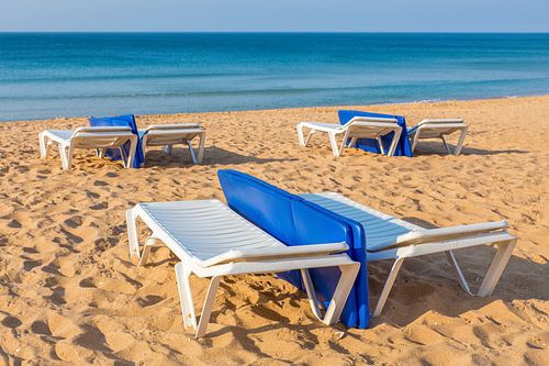 Ligbedden op leeg Portugees strand met blauwe zee