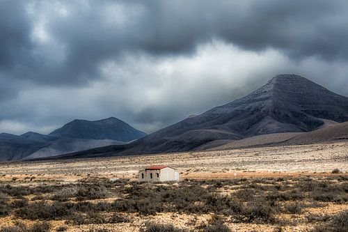 Klein onafgebouwd huisje op een vlakte in een dal met zware lucht.