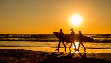 Surfers op het strand vlak voor zonsondergang