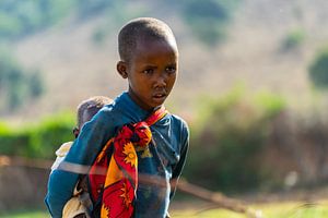Ein Massai-Mädchen mit einem Baby auf dem Rücken.