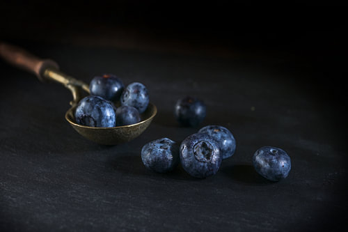 Vintage Messinglöffel mit Blaubeeren auf schwarzer Schieferplatte, dar