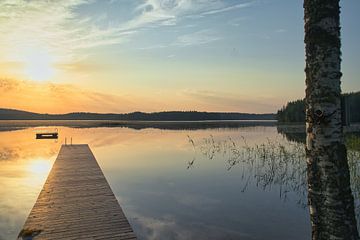 A wooden jetty on the lake in the morning mist, flooded with sunlight and a calm reflection. by Martin Köbsch