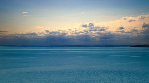 Een rustig zeegezicht onder een heldere hemel. Het water weerspiegelt zachte wolken.