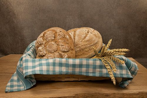 two freshly baked loaves of bread in a wicker basket with a blue and white checkered bread cloth
