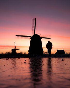 Skater near windmill during colourful winter sunset by Ewold Kooistra