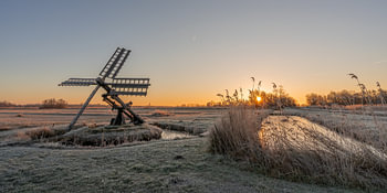 Oude windmolen in een watergebied tijdens zonsopkomst