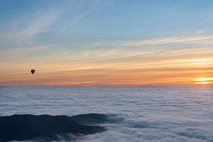 Three hot air balloons flying over a sea of ​​clouds during sunrise. von Carlos Charlez