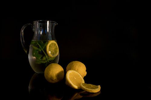 still life with a jug of water filled with mint and lemon with the raw lemon fruit in the foreground