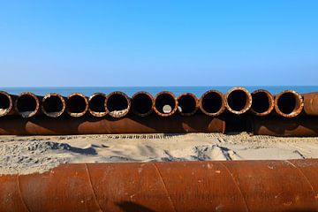 Rust-coloured tubes from a building site in a row at the beach by Studio LE-gals