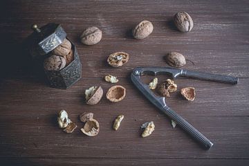 Les noix se trouvent dans une boîte en métal et sur un plateau brun foncé. Certaines noix sont craqu