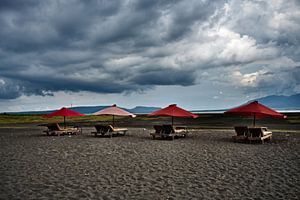 Vulkanischer Strand und dramatisch rote Sonnenschirme
