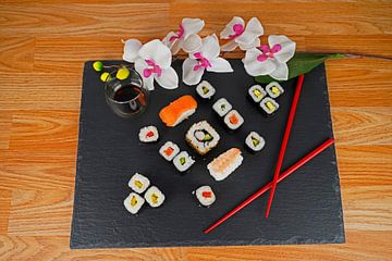 Sushi auf schwarzem Servierteller, serviert mit roten Stäbchen