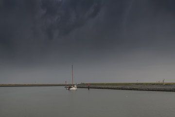 White flat-bottomed sails into the port of Harlingen and a dark sky by Harrie Muis