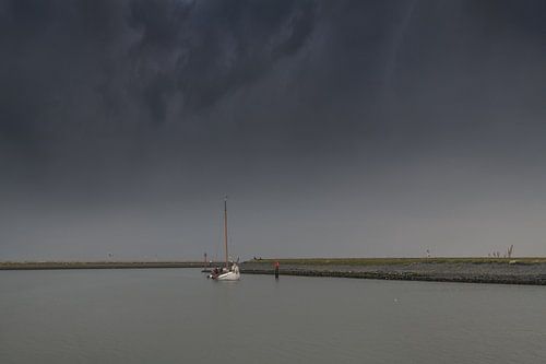 White flat-bottomed sails into the port of Harlingen and a dark sky