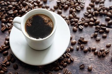 Weiße Tasse mit starkem schwarzem Kaffee auf einem rustikalen Holztisch mit einigen Bohnen, Kopierra