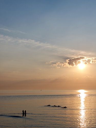 Surfers op zee tijdens zonsondergang