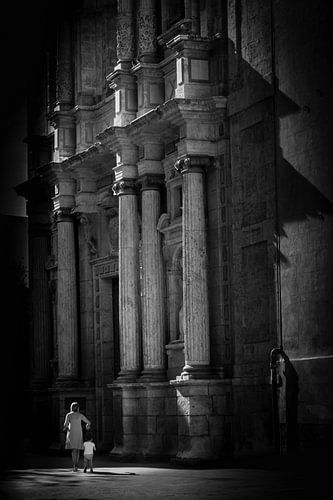 Vrouw en kind in het licht voor de voorgevel van een kerk in zwart-wit