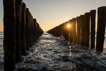 Zonnestralen door de palen in de branding van de zee van Zeeland van Loes Uijtdehaag