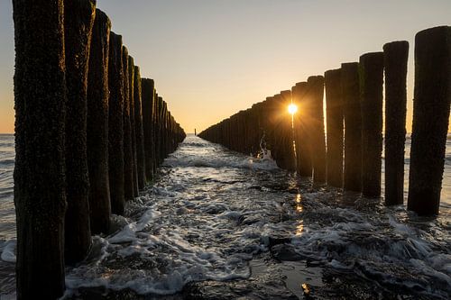 Zonnestralen door de palen in de branding van de zee van Zeeland