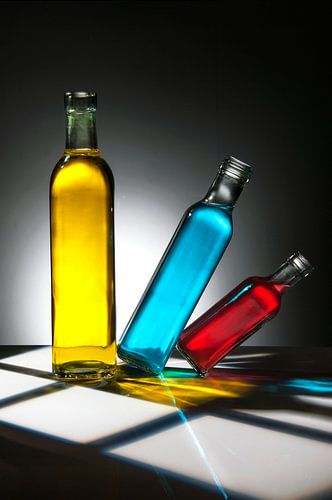 drei Flaschen mit gelber, blauer und roter Flüssigkeit. Die blaue und die rote Flasche stehen schräg.