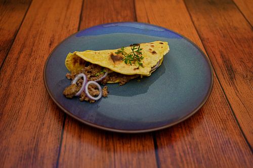 Taco met gehakt-avocado-ui vulling op een bord.