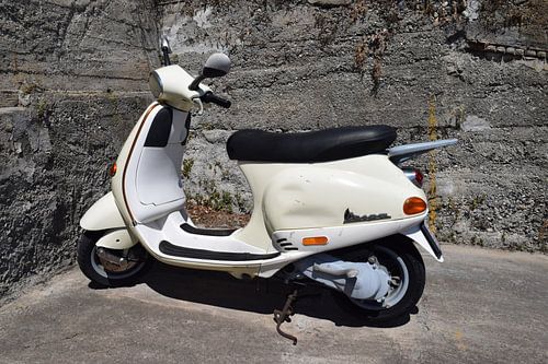 Scooter Vespa classique blanc sous le soleil italien contre un mur de pierre