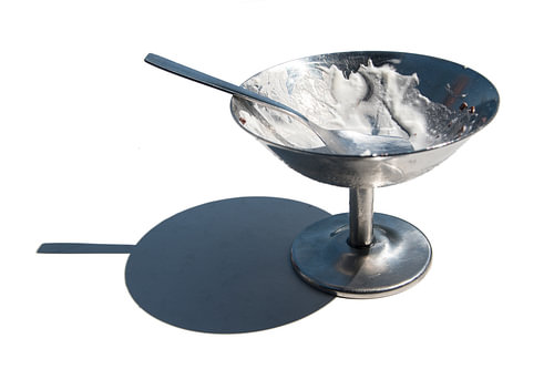 leere Eisbecher aus Metall mit Löffel, der einen scharfen Schatten auf einen weißen Tisch wirft, iso