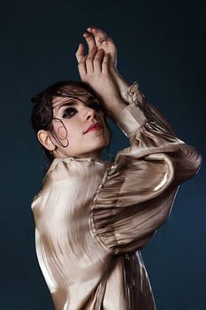 Porträt einer Frau mit goldener Bluse vor blauem Hintergrund