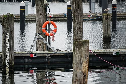 Orangefarbene Rettungsboje oder Rettungsring an einem verwitterten hölzernen Anlegesteg